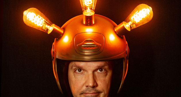 Man met gouden helm met gloeilampen tegen donkere achtergrond.