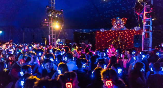 Drukke silent disco met felgekleurde koptelefoons en lichteffecten in een donkere tent