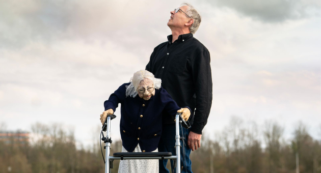 Man die omhoog kijkt en een op leeftijd dame die staat met een rollator