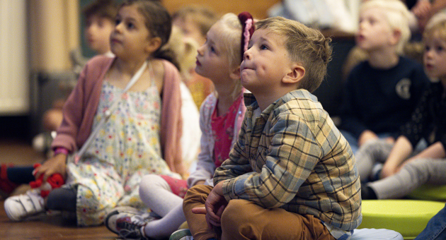 Kinderen die al zitten op de grond geboeid en geconcentreerd zitten te luisteren. 