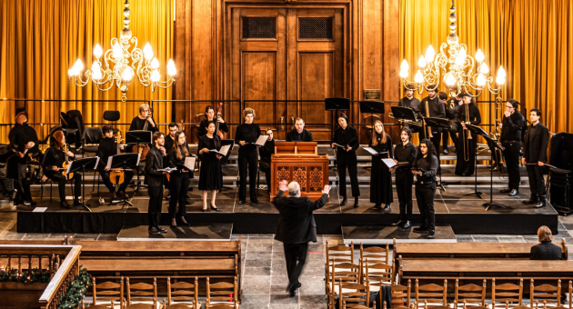 Een klassieke orkest, allemaal gekleed in zwart, treedt op in een sfeervol verlichte houten kerk.