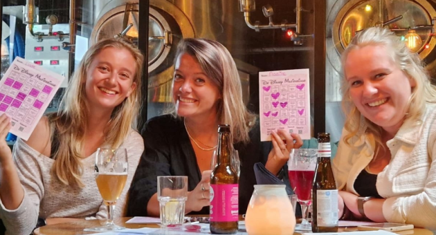 Drie vrouwen lachen met pubquiz formulieren in café