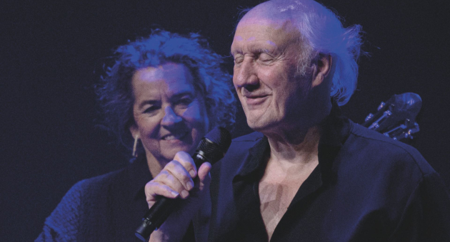 Close-up van Herman van Veen op het podium met een microfoon in zijn hand. 