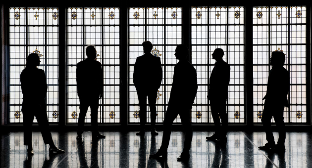 Silhouetten van zes leden van Ensemble Klang voor een monumentaal glas-in-loodraam in een sfeervolle, historische ruimte.