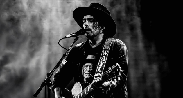 Zanger Waylon met gitaar en hoed zingt in microfoon tijdens liveoptreden