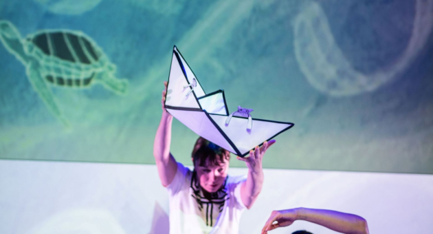 Een fragment van toneelspeler met grote papieren boot boven hoofd.