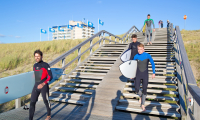 Jongens in wetsuits met surfboarden onder hun arm lopen de houten trap of naar het strand bij Kijkduin