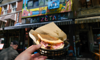 Eine Hand hält ein Sandwich vor einem bunten Restaurant