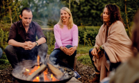 Drei Personen sitzen in der Natur um ein Lagerfeuer.