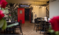 Vue de l'entrée d'une salle de théâtre avec une porte rouge et des tables.