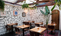 Cozy restaurant featuring artistic wall painting by Jamal Armand and plants.