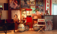 Een sfeervol ingerichte filmtheaterlobby met filmposters aan de muur, een retro popcornmachine, twee discoballen, een witte regisseursstoel met "FLORA" erop, en een medewerker achter de balie.