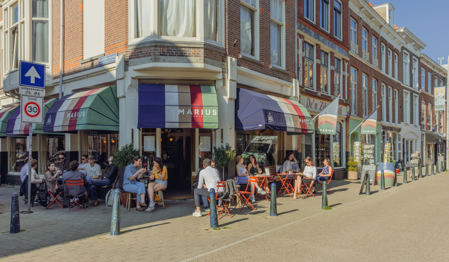 Gezellig druk terras voor een wijnwinkel met gekleurde markiezen in het groen, blauw, wit en rood.