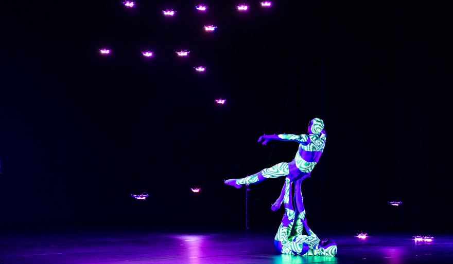 2 performers met lichtgevende pakken op een donker podium 