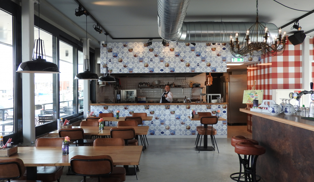Modern interieur met industriële accenten, houten meubilair en open keuken van restaurant Oma Toos in de haven van Scheveningen.