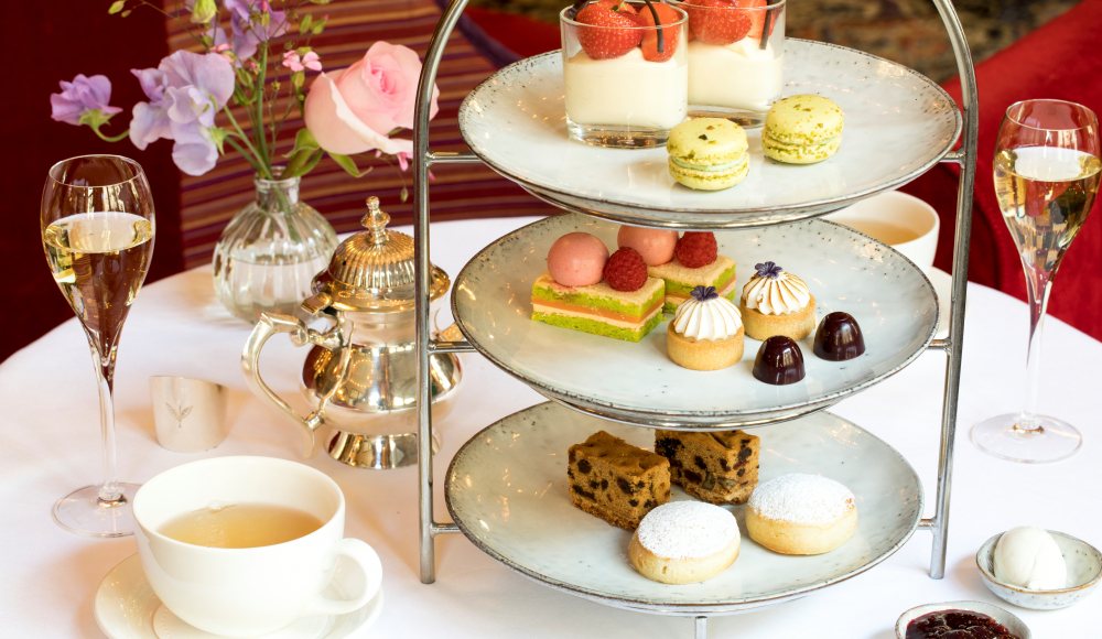 Luxe high tea met etagère vol zoetigheden, thee, champagne en bloemen op een elegant gedekte tafel