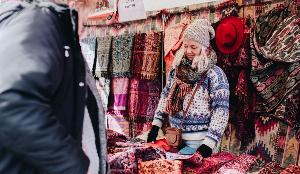 Verkoopster, met muts op en dikke trui achter een kraam met sjaals op Le Marie Marché