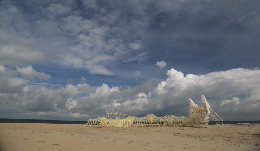 Strandbeest van Theo Jansen te zien op het strand, lucht met veel wolken. 