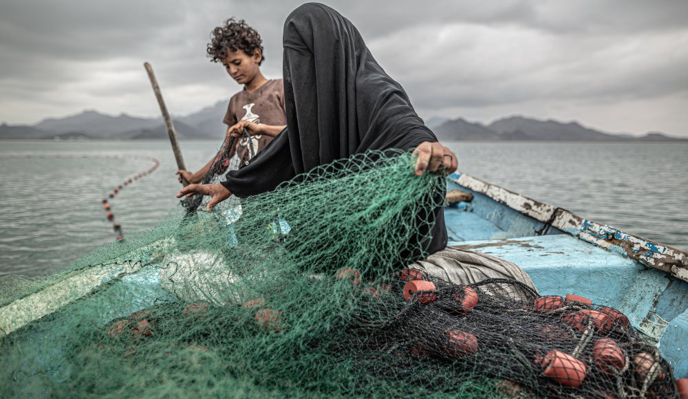 Fatima and her son prepare a fishing net on a boat. Photographer Pablo Tosco Fatima and her son prepare a fishing net on a boat. Photographer Pablo Tosco