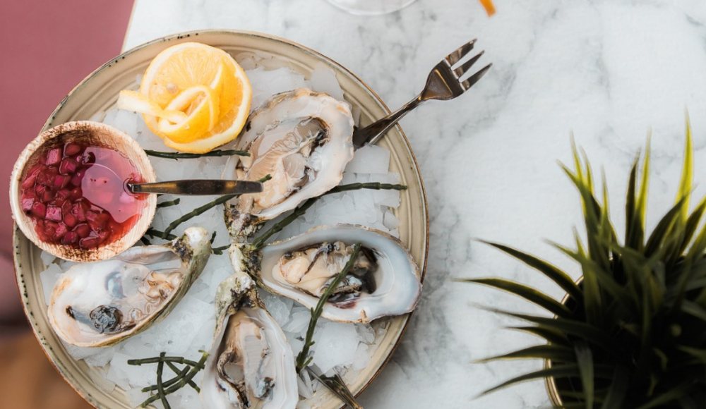 Een kleurrijk opgemaakt plateau met oesters en een heerlijke cocktail ernaast bij Miss Maui Beachhouse