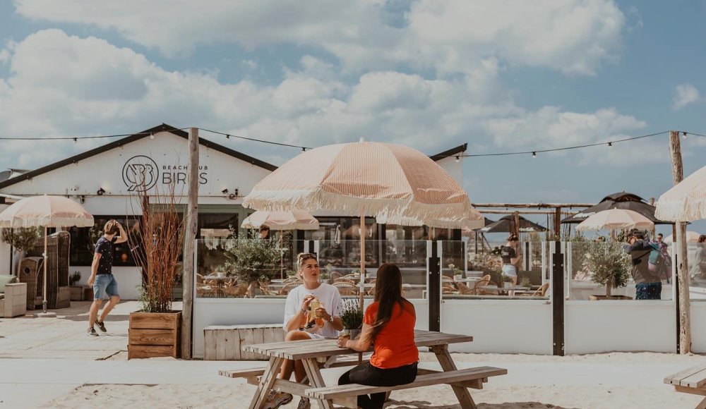 Houten en rieten meubels, jaren 70 parasols op het strand, kortom bij Beachclub Birds beleef je een echte strandvibe.