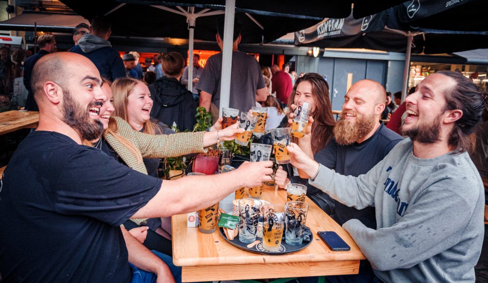 Een groepje lachende mensen die proosten met een biertje bij Kompaan Binnenhaven in het centrum van Den Haag