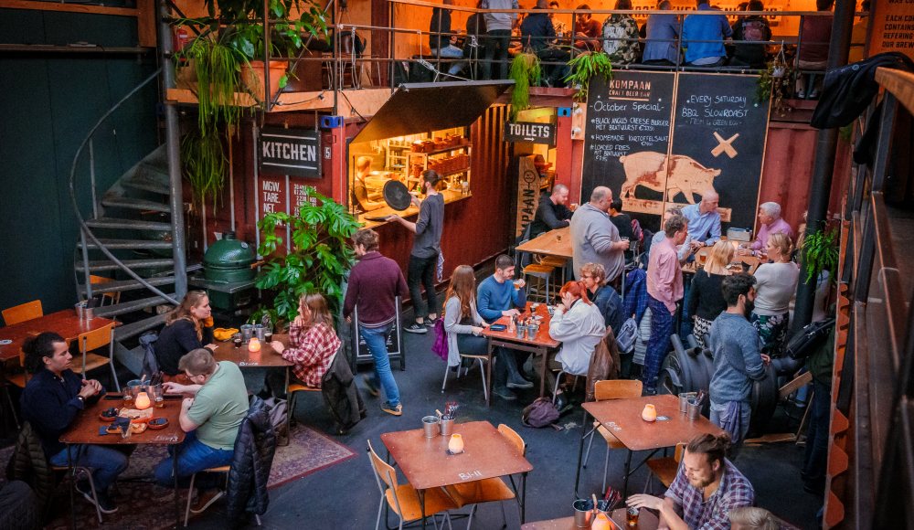 Knusse tafeltjes met mensen die bier drinken in de industriele Kompaan Thuishaven.