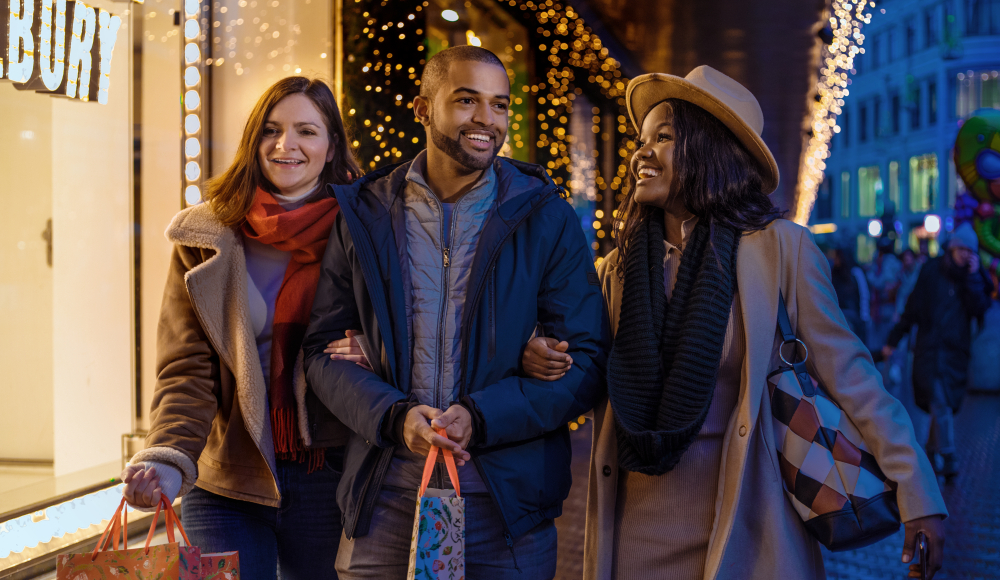 Drie vrienden winkelen samen tijdens de feestdagen in een sfeervol verlichte Grote Marktstraat in Den Haag