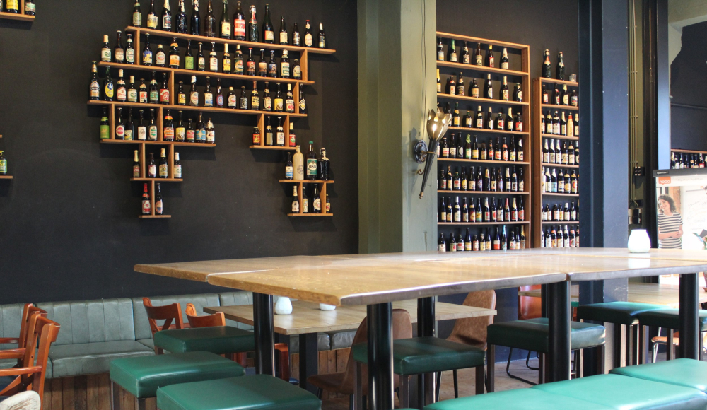 Biertafels bij Brouwerij De Prael met aan de muur een rek met verschillende biertjes.
