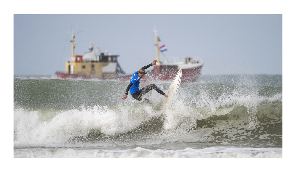 Een surfer op een golf met een boot op de achtergrond
