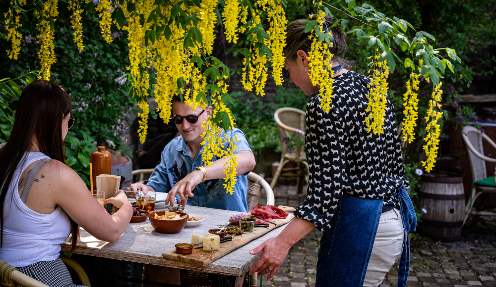 Stelletje aan tafel met gele bloemen waar een borrelplank en likeur geserveert wordt in de tuin Van Kleef