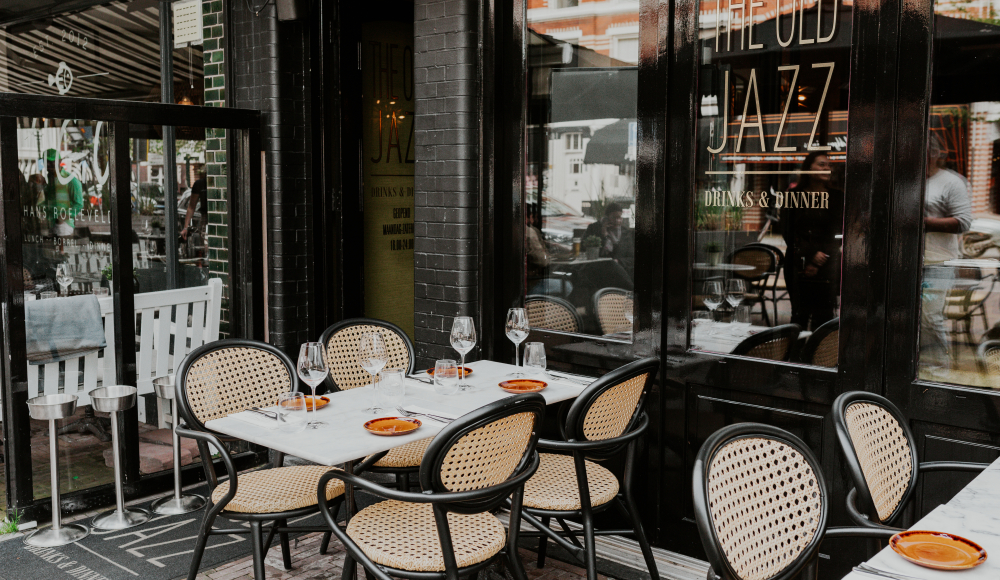 Een sfeervol terras bij Old Jazz, met gedekte tafels, rieten stoelen en een uitnodigende uitstraling, perfect voor een gezellige eetervaring. Een sfeervol terras bij Old Jazz, met gedekte tafels, rieten stoelen en een uitnodigende uitstraling, perfect voor een gezellige eetervaring.