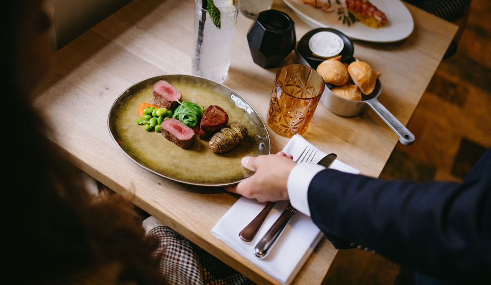 De ober serveert een prachtig opgemaakt bord uit. Een signature dish van de chef, een "klein kunstwerk". 