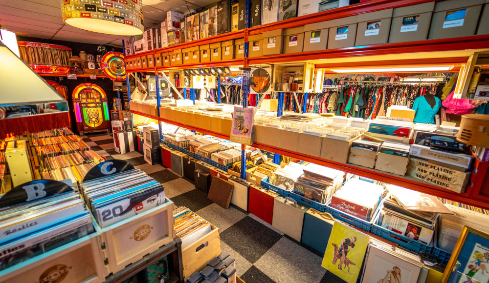 Retro muziek- en platenwinkel met vinylbakken, kleurrijke jukeboxen en vintage muziekmemorabilia, waaronder Elvis Presley-platen en gouden records. Retro muziek- en platenwinkel met vinylbakken, kleurrijke jukeboxen en vintage muziekmemorabilia, waaronder Elvis Presley-platen en gouden records.