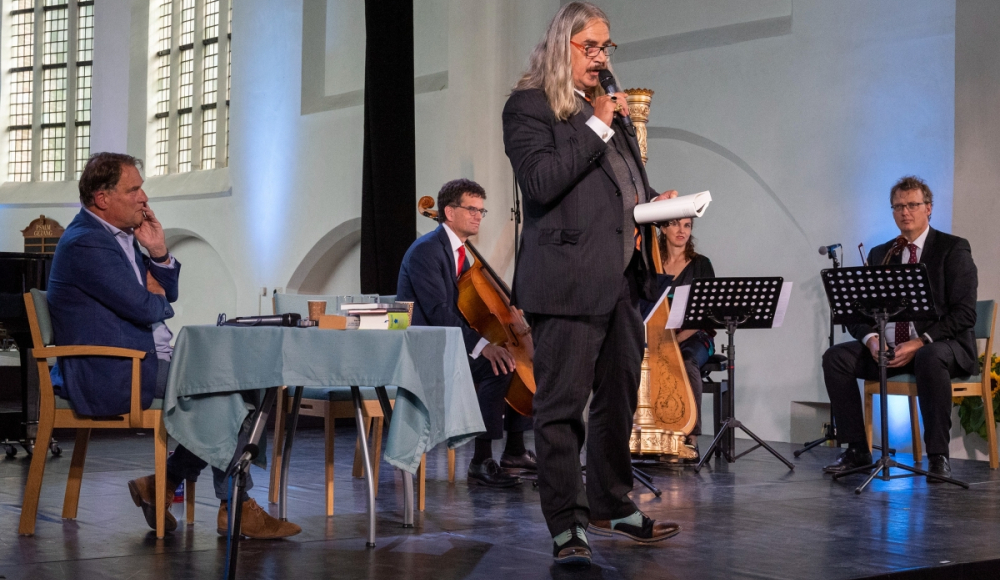 Spreker met microfoon en muzikanten tijdens Huygens Festival (c) Huygens Festival Spreker met microfoon en muzikanten tijdens Huygens Festival (c) Huygens Festival