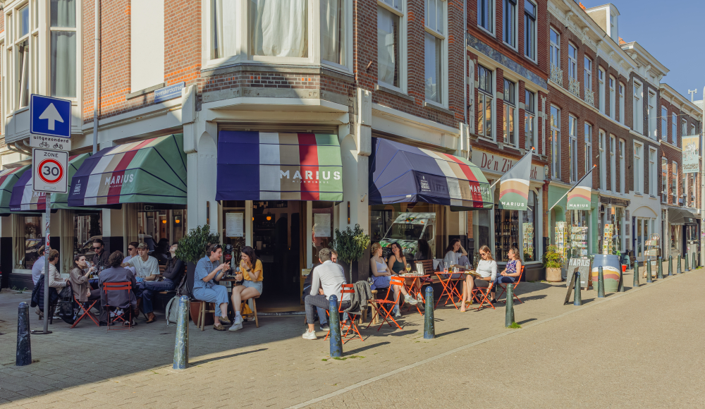 Gezellig druk terras voor een wijnwinkel met gekleurde markiezen in het groen, blauw, wit en rood.
