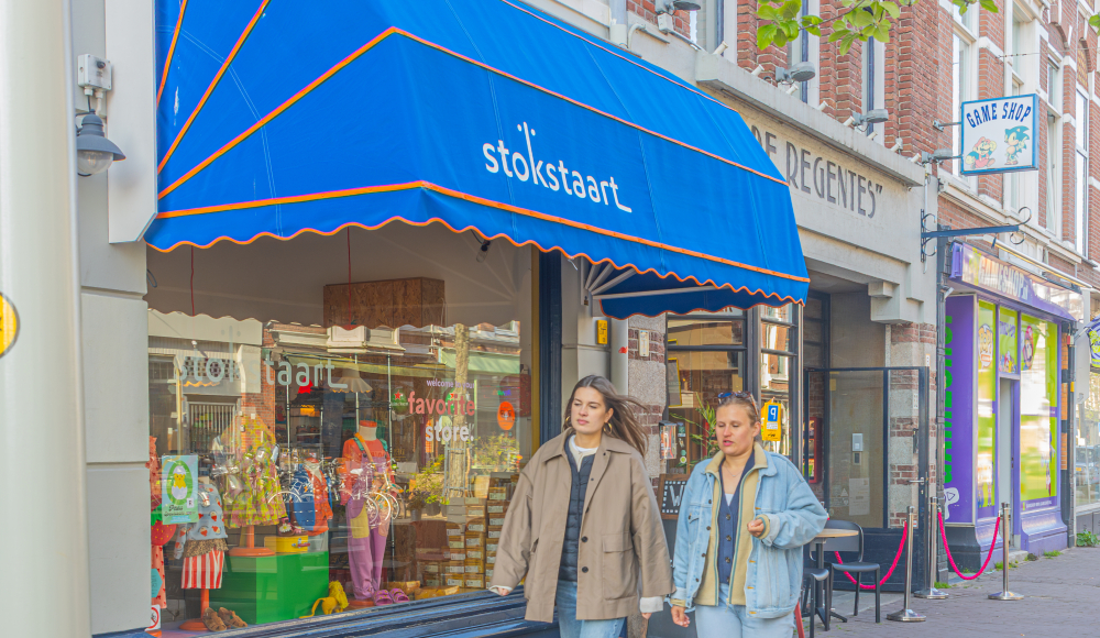 Twee mensen lopen over straat, achter hen een blauwe markies