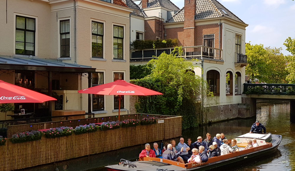 Rondvaart met groep langs terras aan Haagse gracht.