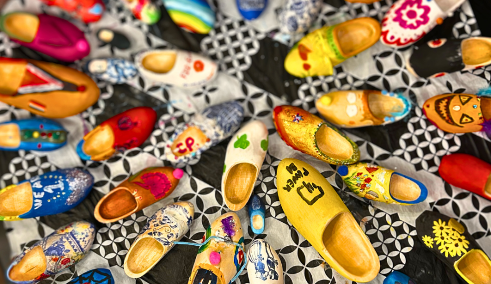 Versierde klompen in allerlei kleuren en patronen, creatief uitgestald op een zwart-wit tafelkleed in een cirkelvormige opstelling. Versierde klompen in allerlei kleuren en patronen, creatief uitgestald op een zwart-wit tafelkleed in een cirkelvormige opstelling.