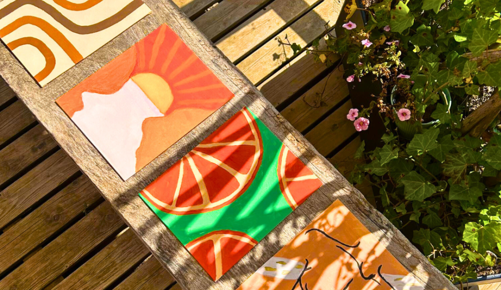 Zes kleurrijke schilderijtjes op houten tafel in zon.
