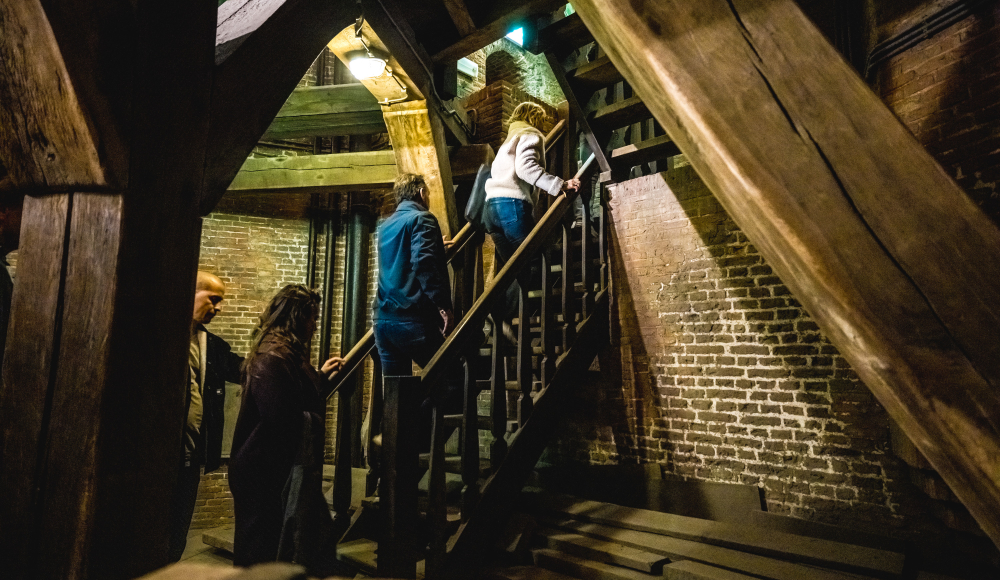 Bezoekers beklimmen trap in historische torenruimte.