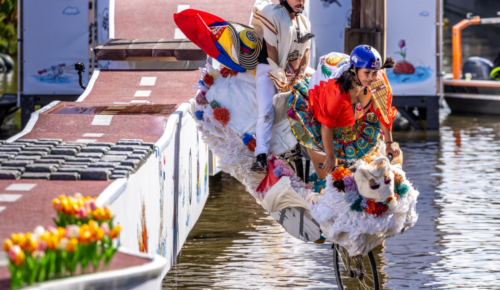 Twee deelnemers in kleurrijke kostuums vliegen met hun zelfgemaakte fiets de lucht in tijdens Red Bull Showrun boven een Haagse gracht. Twee deelnemers in kleurrijke kostuums vliegen met hun zelfgemaakte fiets de lucht in tijdens Red Bull Showrun boven een Haagse gracht.