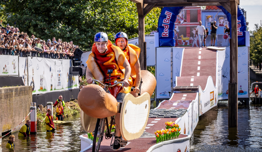 Twee deelnemers verkleed als hotdog racen op een creatief voertuig van de schans tijdens Red Bull Showrun in Den Haag. Twee deelnemers verkleed als hotdog racen op een creatief voertuig van de schans tijdens Red Bull Showrun in Den Haag.