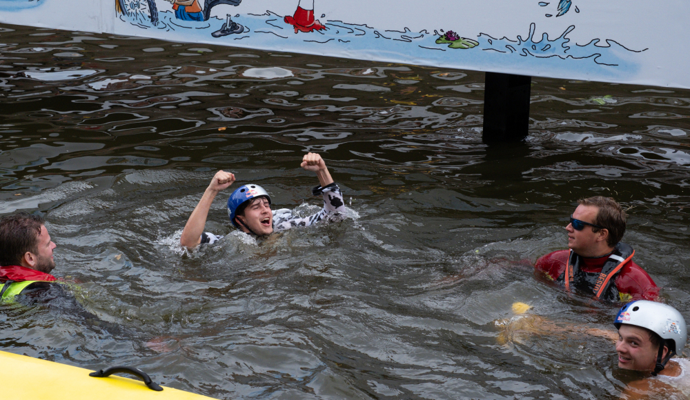 Een deelnemer juicht in het water na een spectaculaire landing tijdens Red Bull Stalen Ros in Den Haag, omringd door hulpverleners. Een deelnemer juicht in het water na een spectaculaire landing tijdens Red Bull Stalen Ros in Den Haag, omringd door hulpverleners.
