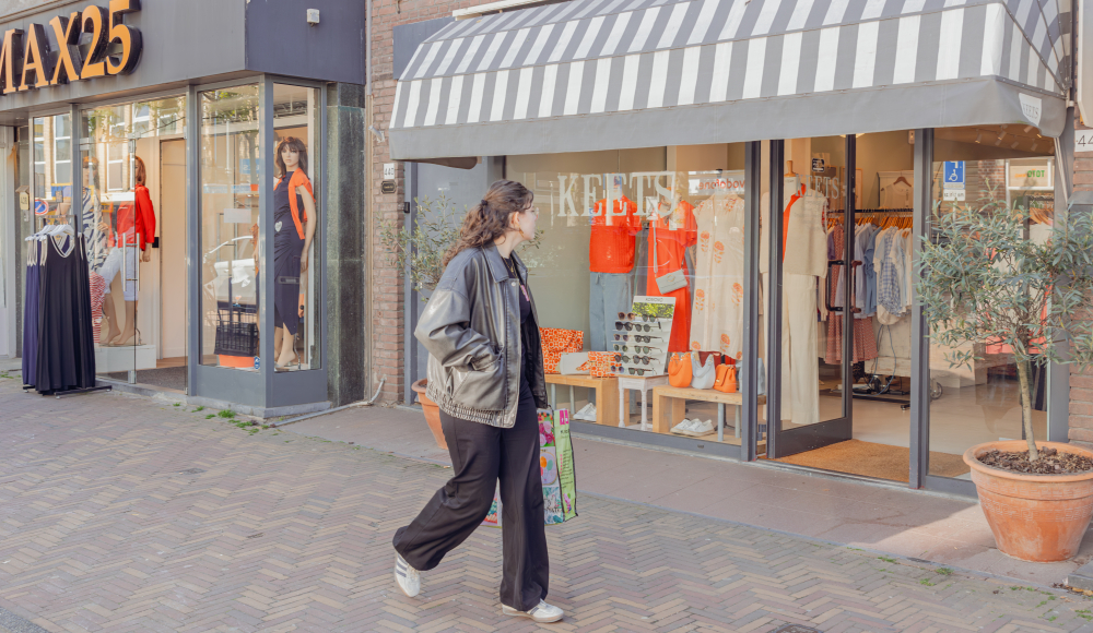 Vrouw loopt langs een winkelpand met een markies en een etalage met rode kleding