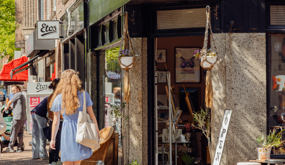 Vrouw loopt door een straat langs een open winkel.