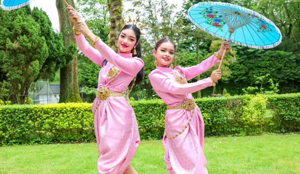Twee dames in traditionele kleding in Thaise danspose met papieren parasols omhoog wijzend. Twee dames in traditionele kleding in Thaise danspose met papieren parasols omhoog wijzend.