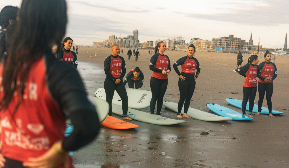 Surfers in wetsuits met surfplanken in de branding krijgen uitleg op het strand. Surfers in wetsuits met surfplanken in de branding krijgen uitleg op het strand.