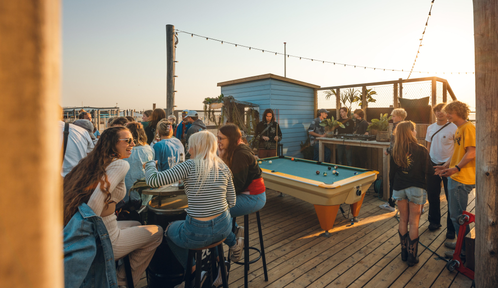 Hartbeach terras met veel gasten aan tafels en pooltafel die genieten van de surfcultuur Foto: Zajicek Hartbeach terras met veel gasten aan tafels en pooltafel die genieten van de surfcultuur Foto: Zajicek