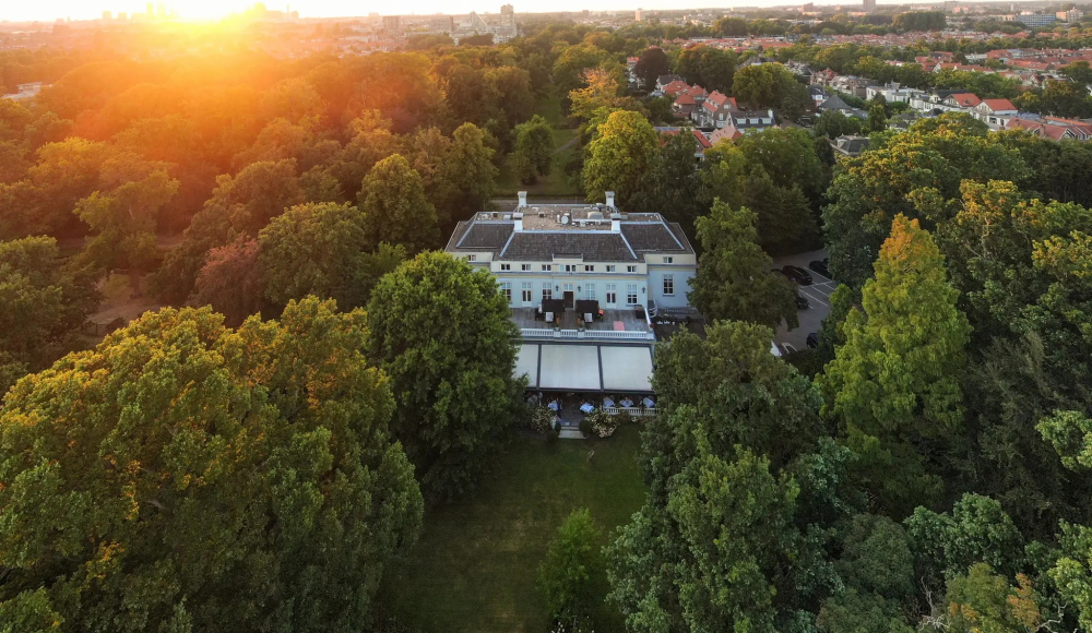 Luchtfoto van wit landhuis in Den Haag, omringd door bomen en park bij zonsondergang